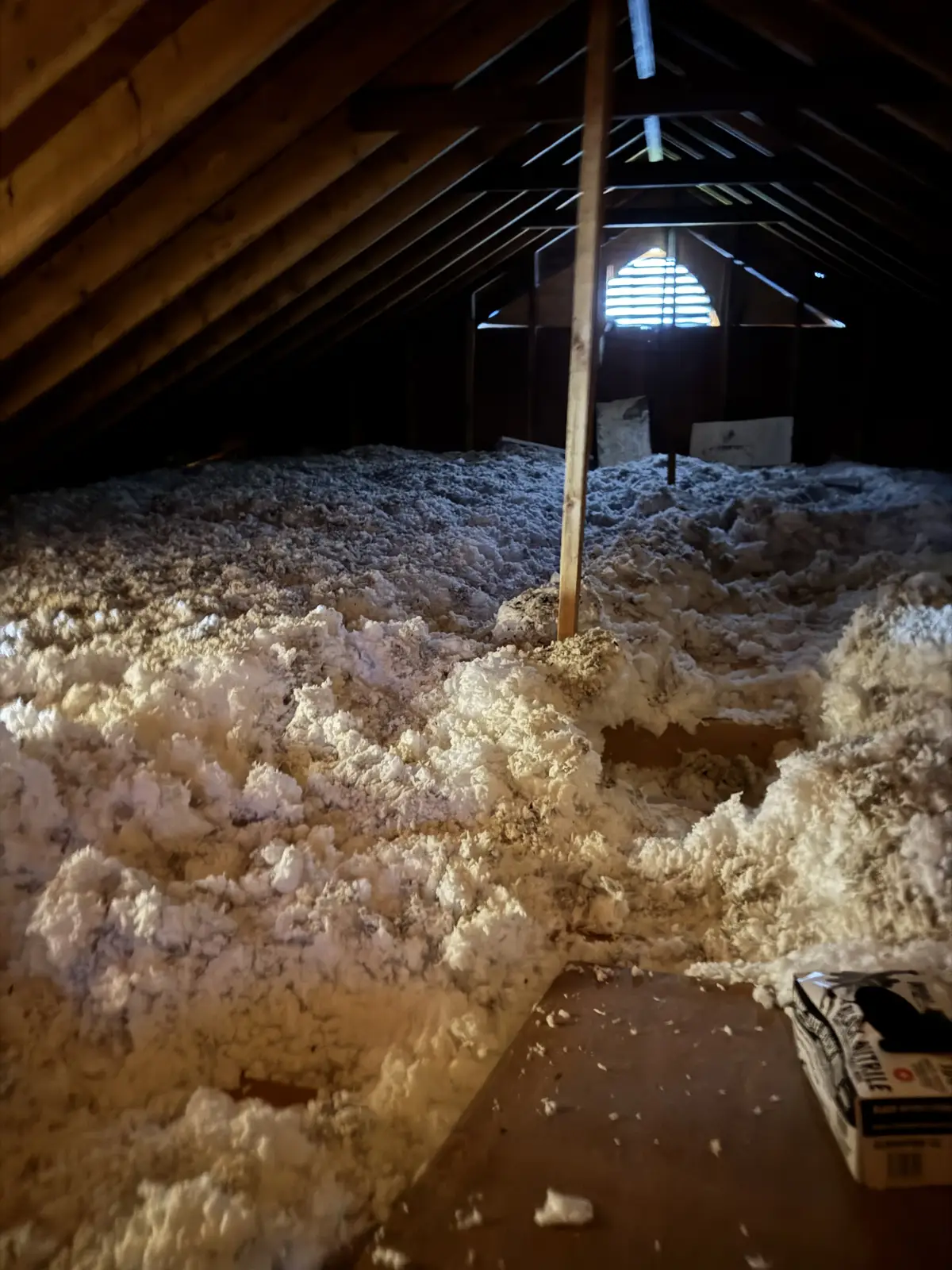 Old blown-in insulation heaped unevenly across an attic floor